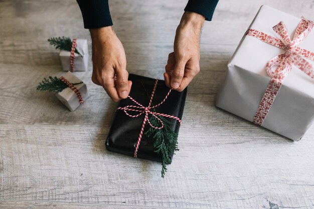 Hombre atar arco en caja de regalo negro con rama de ciprés