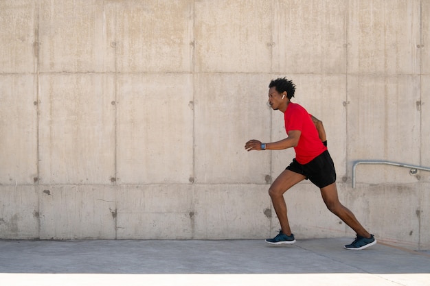 Hombre atlético afro corriendo y haciendo ejercicio al aire libre en la calle. Concepto de deporte y estilo de vida saludable.