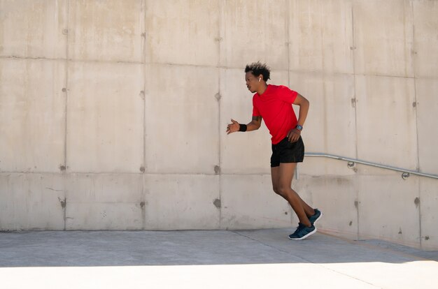 Hombre atlético afro corriendo y haciendo ejercicio al aire libre en la calle