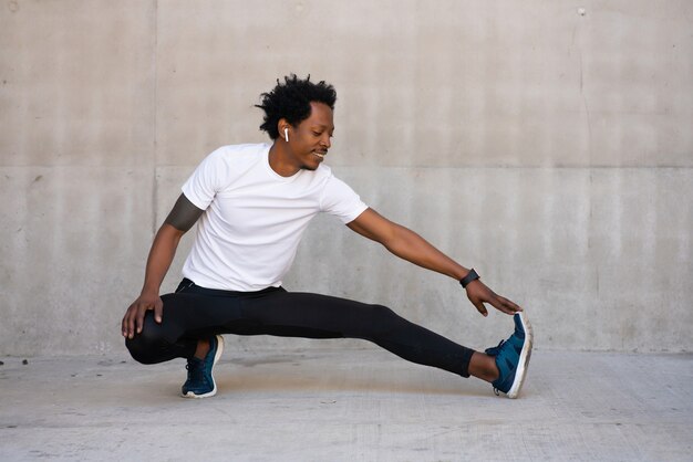 Hombre atlético afro estirando las piernas y calentando antes de hacer ejercicio al aire libre. Concepto de deporte y estilo de vida saludable.