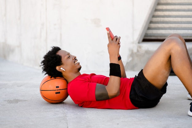 Hombre atlético afro usando su teléfono móvil y relajarse después de hacer ejercicio al aire libre