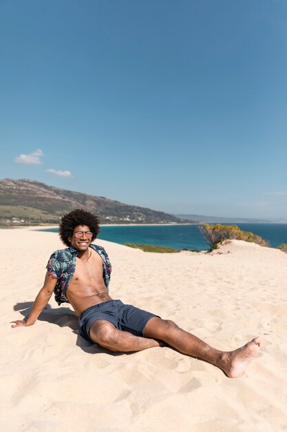 Hombre atlético joven que se sienta en la playa arenosa