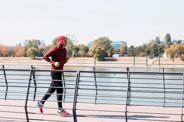 Hombre atlético joven en la sudadera con capucha de la sudadera que corre en el parque