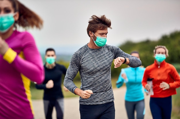 Hombre atlético revisando su frecuencia cardíaca en un reloj inteligente mientras participa en una maratón durante la epidemia de virus