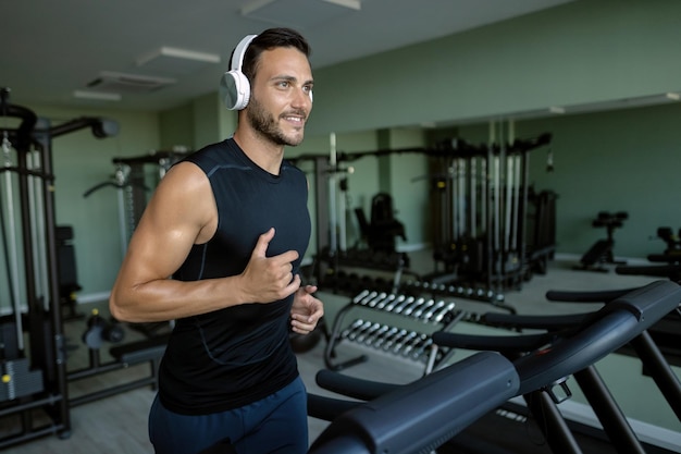 Hombre atlético sonriente corriendo en una caminadora mientras hace ejercicio en un gimnasio