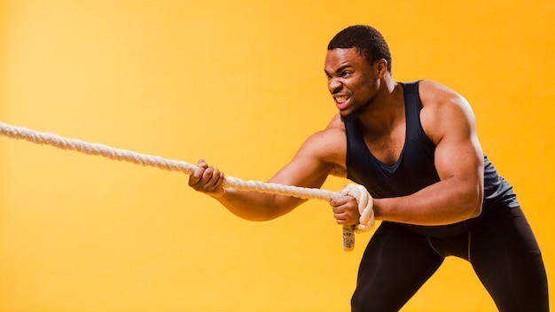 Hombre atlético en traje de gimnasio tirando de la cuerda