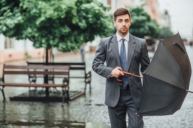 Foto gratuita hombre atractivo va por la calle con paraguas y mira al frente