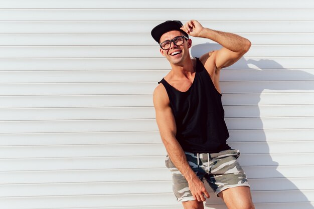 Foto gratuita hombre atractivo divertido en anteojos posando cerca de la pared urbana, vistiendo camiseta negra