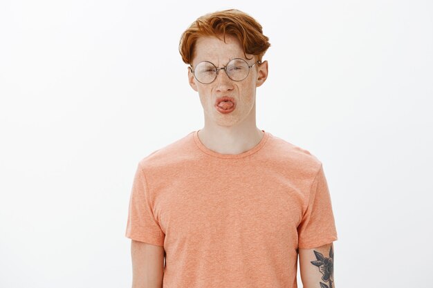 Hombre atractivo pelirrojo tonto en gafas mostrando lengua