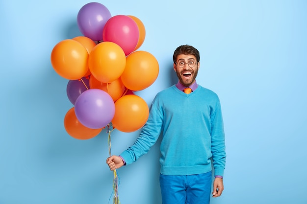 Hombre atractivo positivo con mirada feliz, lleva gafas redondas, traje azul