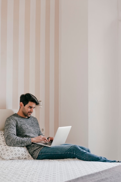 Hombre atractivo usando la computadora portátil en la cama