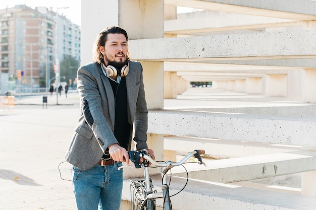 Foto gratuita un hombre con auriculares alrededor de su cuello parado cerca de la bicicleta.