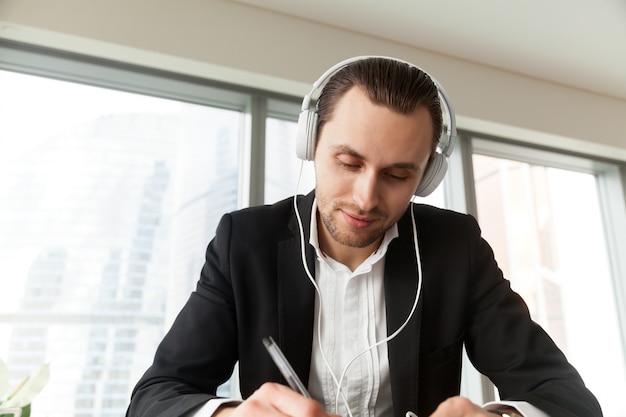 Foto gratuita hombre en auriculares escribiendo con pluma en el escritorio de trabajo