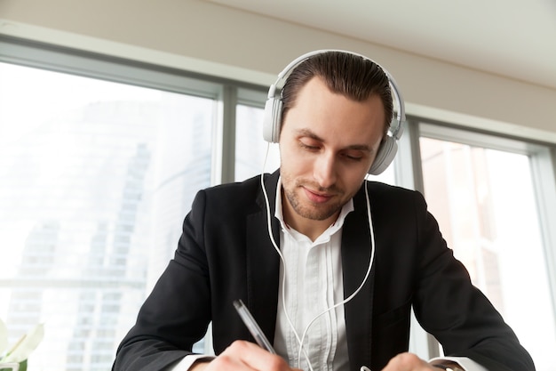 Hombre en auriculares escribiendo con pluma en el escritorio de trabajo