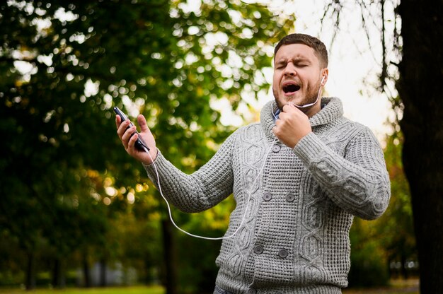 Hombre con auriculares en los oídos cantando en el parque