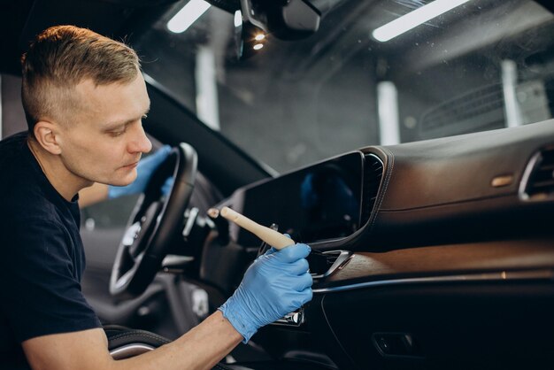 El hombre en el auto limpia usando un cepillo para limpiar todos los detalles dentro del vehículo