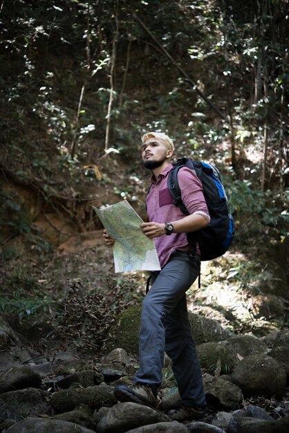 Hombre de la aventura que observa el mapa en una trayectoria de la montaña para encontrar la manera correcta.