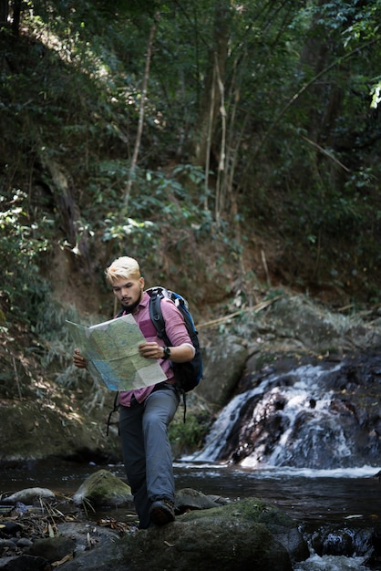 Hombre de la aventura que observa el mapa en una trayectoria de la montaña para encontrar la manera correcta.