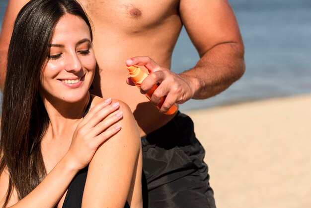 Hombre ayudando a la mujer a aplicar protector solar en la playa.