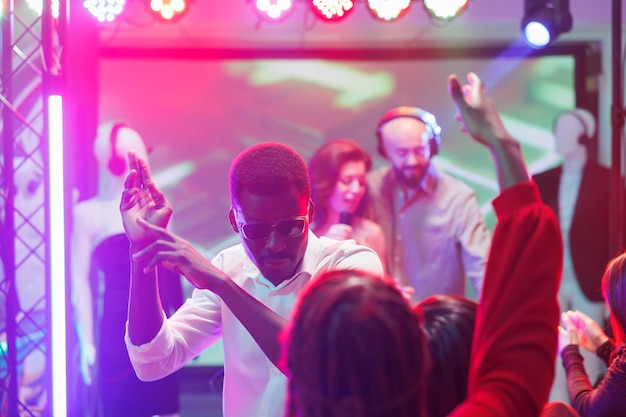 Foto gratuita hombre bailando con amigos y de fiesta en discoteca en club nocturno. joven clubber afroamericano divirtiéndose y haciendo movimientos en la pista de baile en un concierto de música electrónica en el club