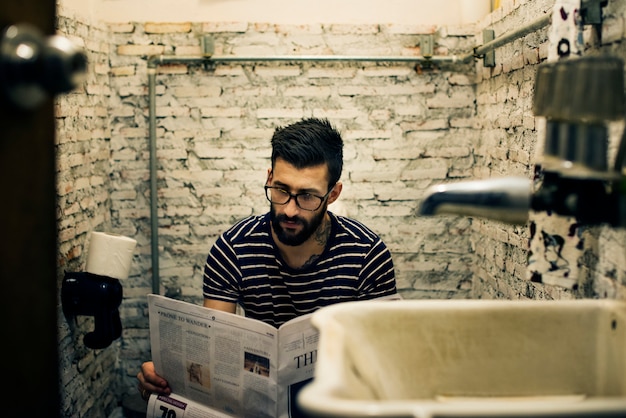 Foto gratuita hombre en un baño leyendo un periódico