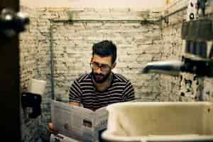 Foto gratuita hombre en un baño leyendo un periódico