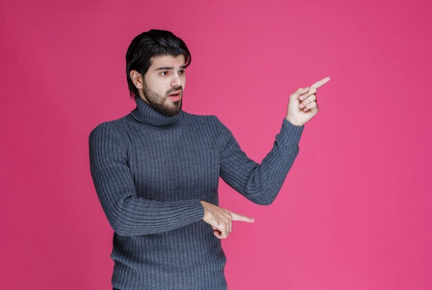 Hombre con barba apuntando a algo o presentando a alguien.