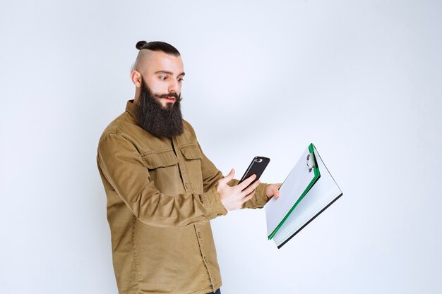 Hombre con barba comprobando los informes contables y calculando en el teléfono.