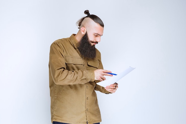 Foto gratuita hombre con barba comprobando la lista de proyectos y marcando notas o correcciones.