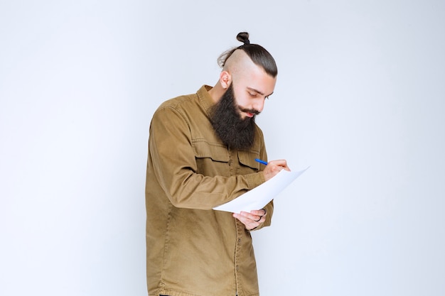 Hombre con barba comprobando la lista de proyectos y marcando notas o correcciones.