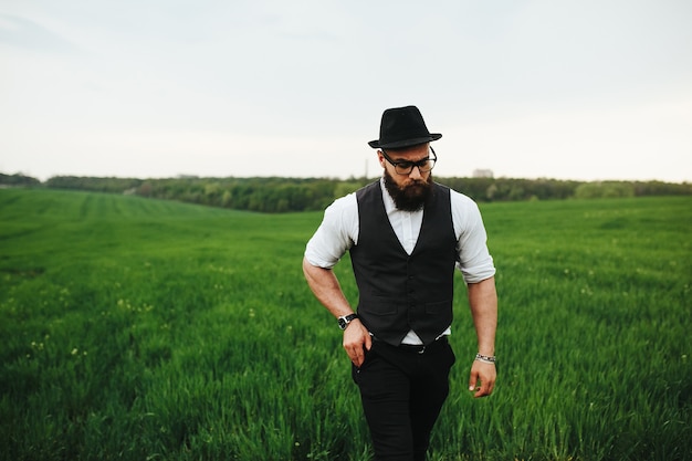 Un hombre con barba y gafas de sol caminando por el campo.