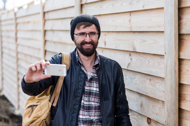 Hombre de barba hipster alegre sonriendo y haciendo autorretrato con teléfono móvil