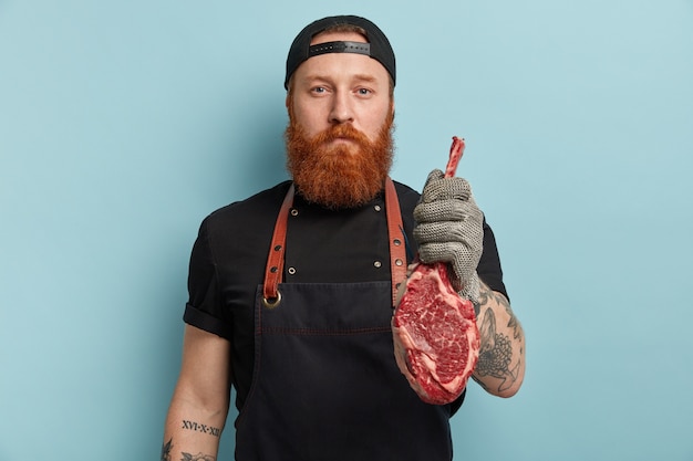 Foto gratuita hombre con barba de jengibre en delantal y guantes con carne