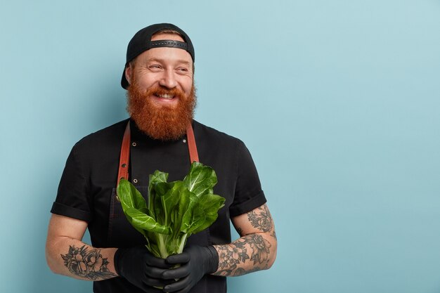 Hombre con barba de jengibre en delantal y guantes con ensalada