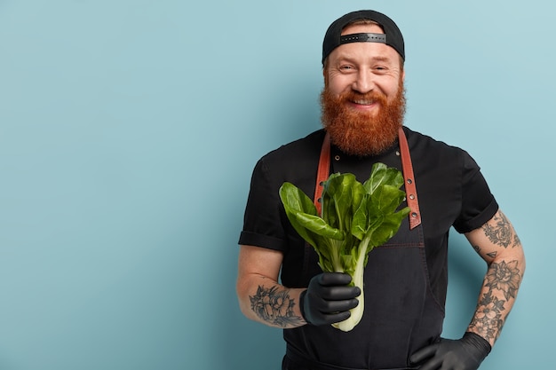 Hombre con barba de jengibre en delantal y guantes con ensalada