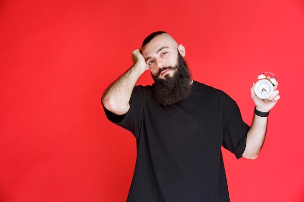 Foto gratuita hombre con barba mostrando despertador y durmiendo.