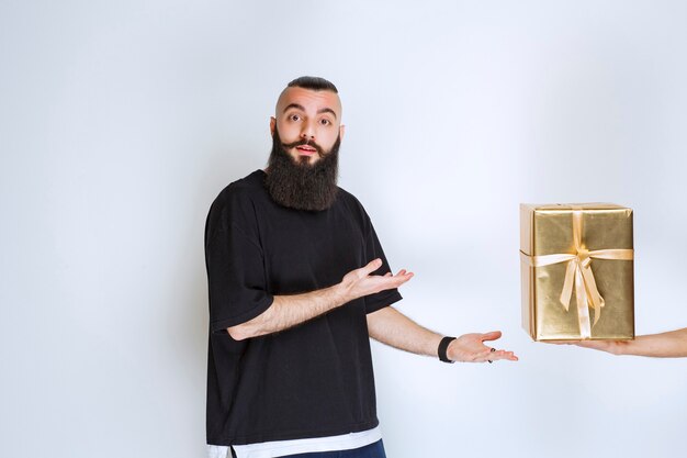 Hombre con barba mostrando su caja de regalo de envoltura dorada.