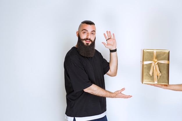 Hombre con barba mostrando su caja de regalo de envoltura dorada.