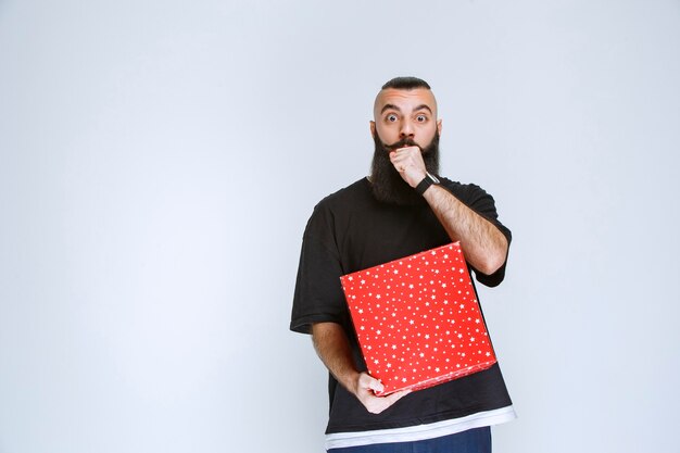 Hombre con barba mostrando su caja de regalo roja.