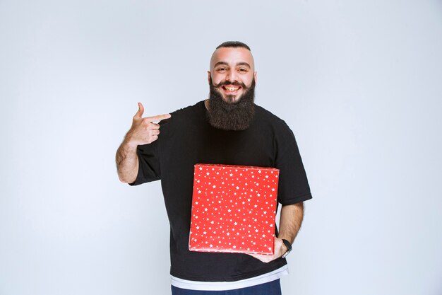 Hombre con barba mostrando su caja de regalo roja.