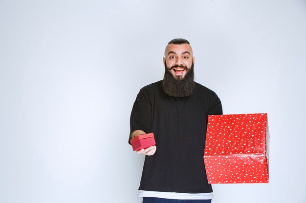 Foto gratuita hombre con barba ofreciendo caja de regalo roja