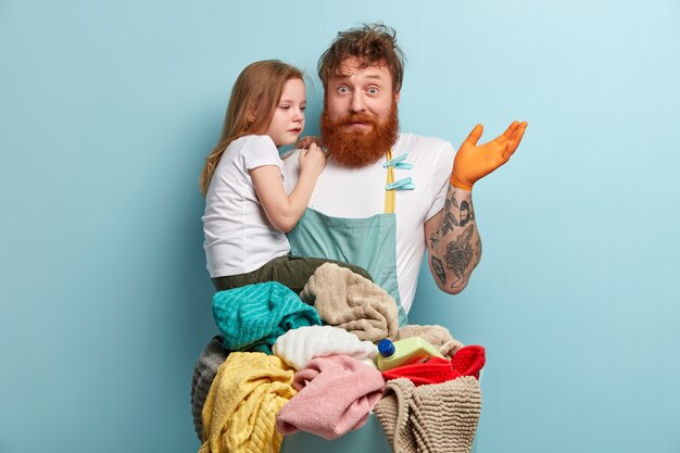 Hombre con barba pelirroja lavando ropa y sosteniendo a su hija