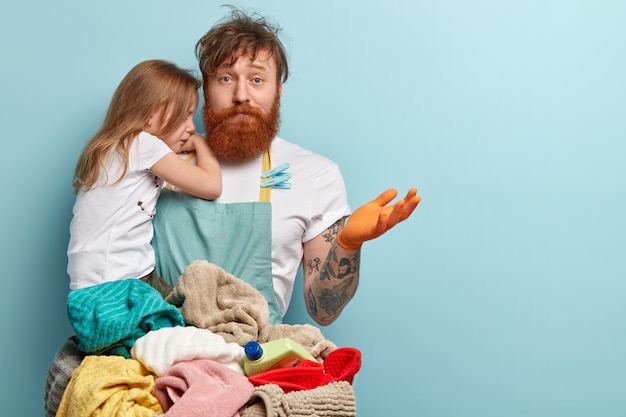 Hombre con barba pelirroja sosteniendo a su hija y lavando ropa