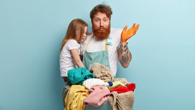 Hombre con barba pelirroja sosteniendo a su hija y lavando ropa