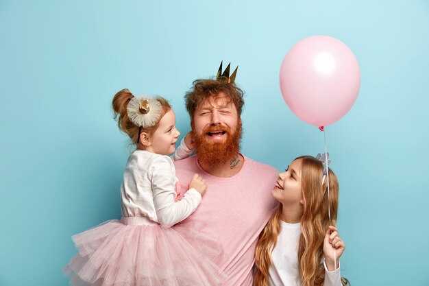 Hombre con barba pelirroja y sus hijas con accesorios de fiesta