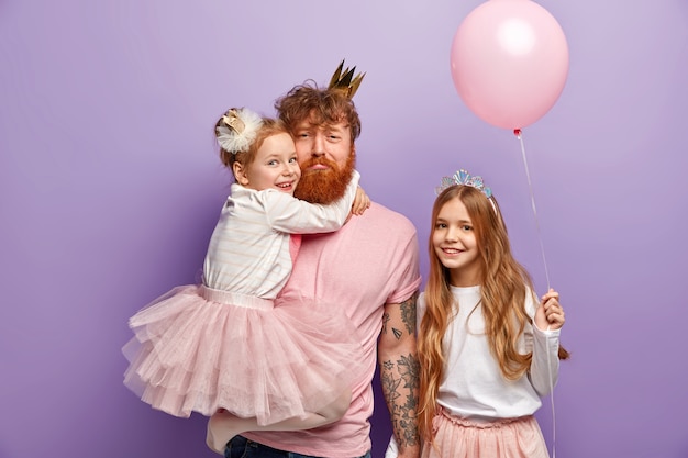 Hombre con barba pelirroja y sus hijas con accesorios de fiesta