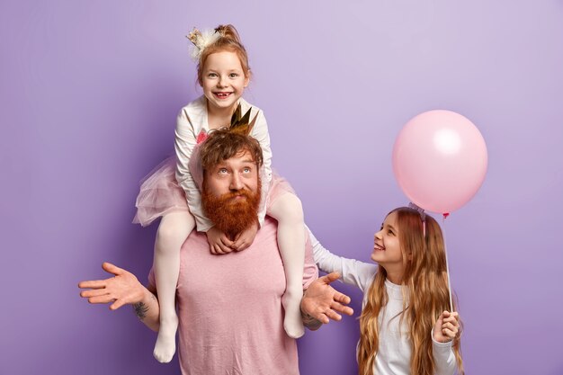 Hombre con barba pelirroja y sus hijas con accesorios de fiesta