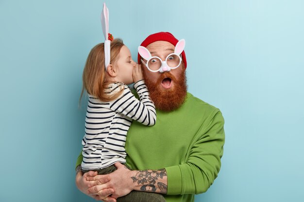 Hombre con barba pelirroja vistiendo ropas coloridas y sosteniendo a su hija