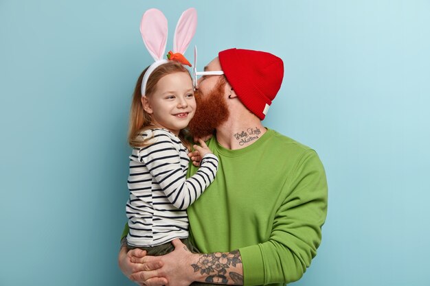 Hombre con barba pelirroja vistiendo ropas coloridas y sosteniendo a su hija