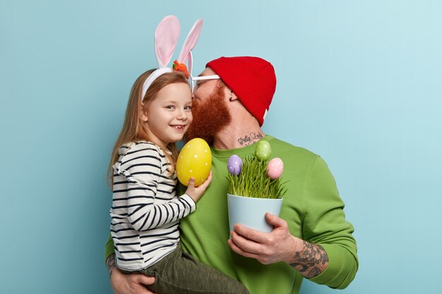 Hombre con barba pelirroja vistiendo ropas coloridas y sosteniendo a su hija